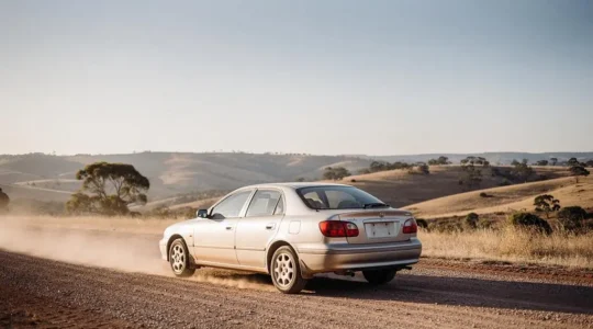 A two-wheel-drive car navigating a sunlit gravel and dirt track through open countryside, symbolizing confident driving without four-wheel drive.