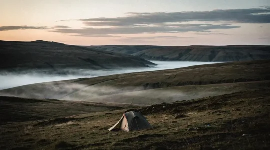 A small, low-profile tent nestled alone in a vast, empty wilderness landscape at dusk, symbolizing true isolation away from human activity.