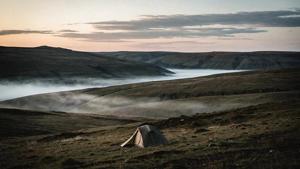 A small, low-profile tent nestled alone in a vast, empty wilderness landscape at dusk, symbolizing true isolation away from human activity.