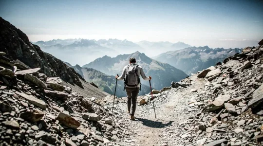 Hiker using a pair of trekking poles while descending a steep rocky mountain trail at golden hour