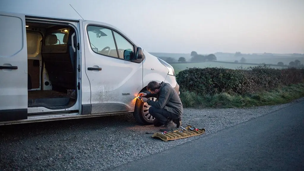A weathered white panel van parked at dawn on a rural roadside, being inspected before a camper conversion project.