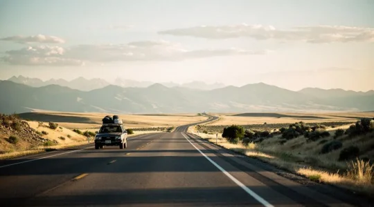 A car driving on a long open highway toward distant mountains at golden hour, symbolizing a three-week road expedition