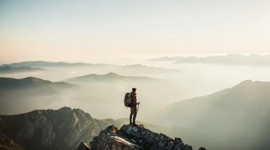 A solitary traveler standing at the edge of a quiet, mist-covered natural viewpoint at dawn, symbolizing the search for authentic, uncrowded travel experiences.